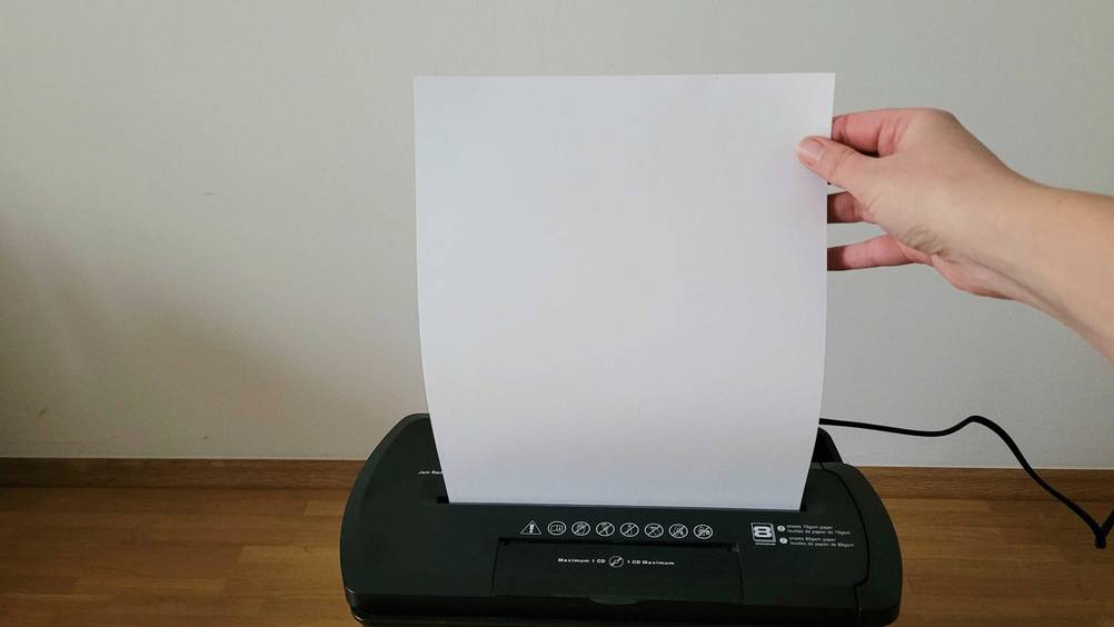 Getestet: Eine Hand hält ein Papier das in den Aktenvernichter eingeführt wird.