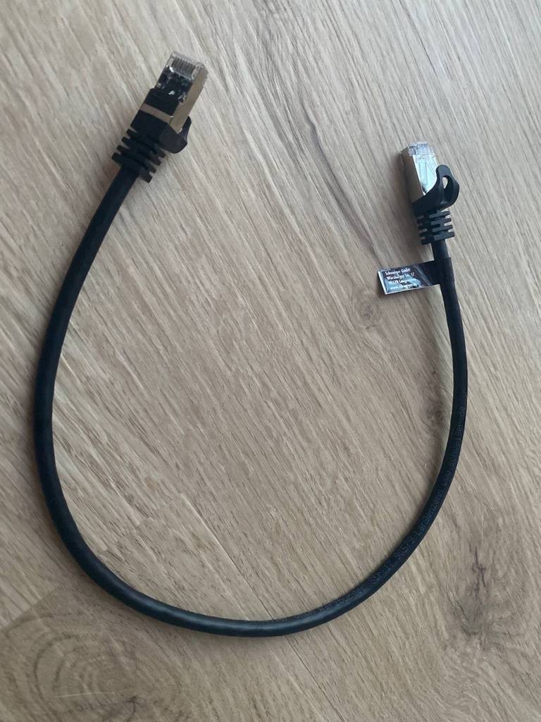 Kurzes, schwarzes, getestetes Netzwerkabel Amazon Basics cat7 liegt auf einem Holzuntergrund.