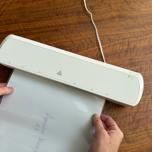 Zwei Hände schieben ein Blatt zum Laminieren in das Amazon-Basics-Thermo-Laminiergerät