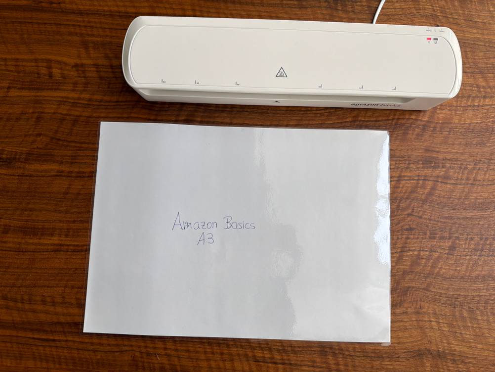Ein laminiertes Blatt liegt neben dem Amazon-Basics-Thermo-Laminiergerät