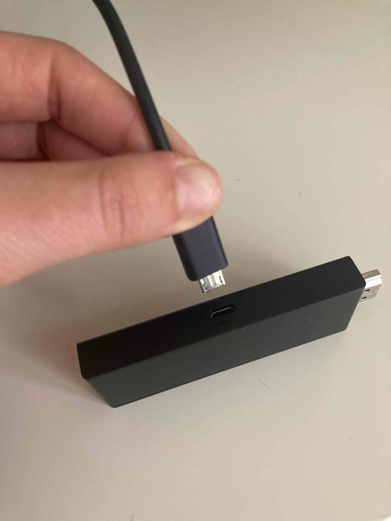 Vor einem hellen Hintergrund hält eine Hand ein USB-Kabel, um daran den darunterliegenden Amazon-Fire-Tv-Stick im Test anzuschließen.