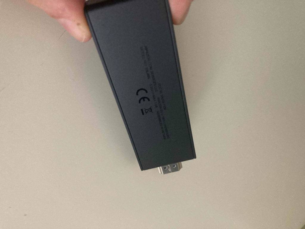Zwei Finger halten einen getesteten Amazon-Fire-Tv-Stick vor beigefarbenem Hintergrund.