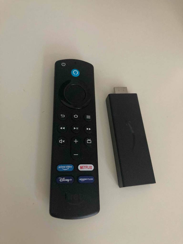 Ein Amazon-Fire-Tv-Stick im Test liegt neben der dazugehörigen Fernbedienung auf einer hellen Fläche.