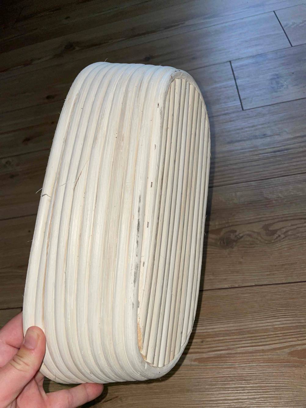 Im Test: Boden eines länglichen Gärkörbchen von einer Hand vor einen Holzboden gehalten.
