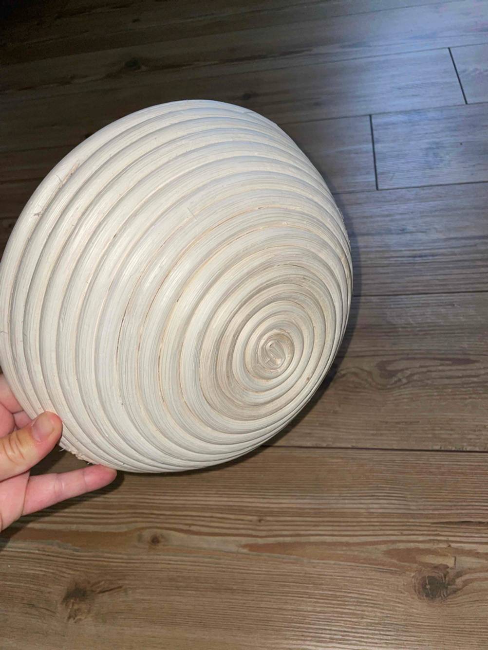 Boden eines runden Gärkörbchen im Test von einer Hand vor einen Holzboden gehalten.