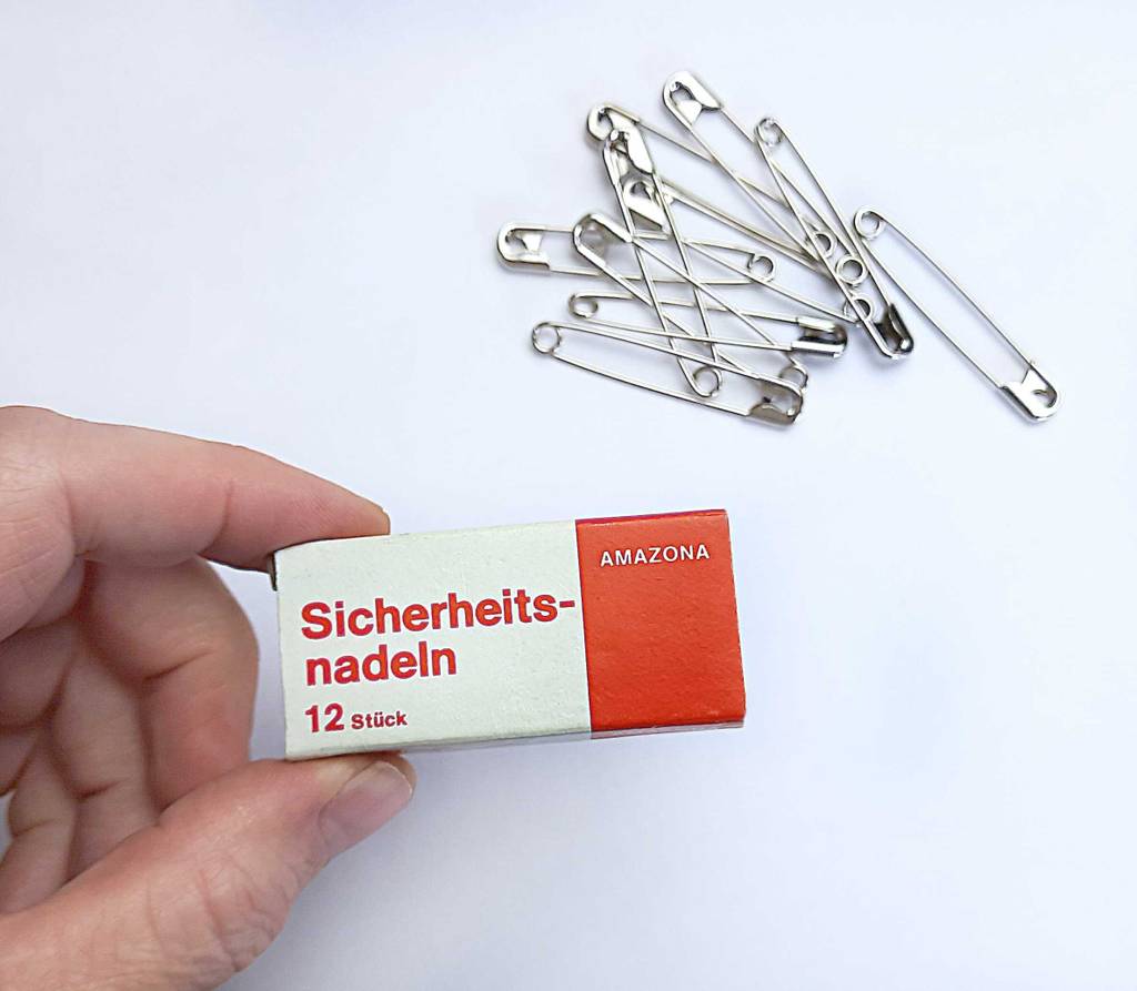 Im Test: Eine Hand hält die Verpackung über einem Haufen Sicherheitsnadeln