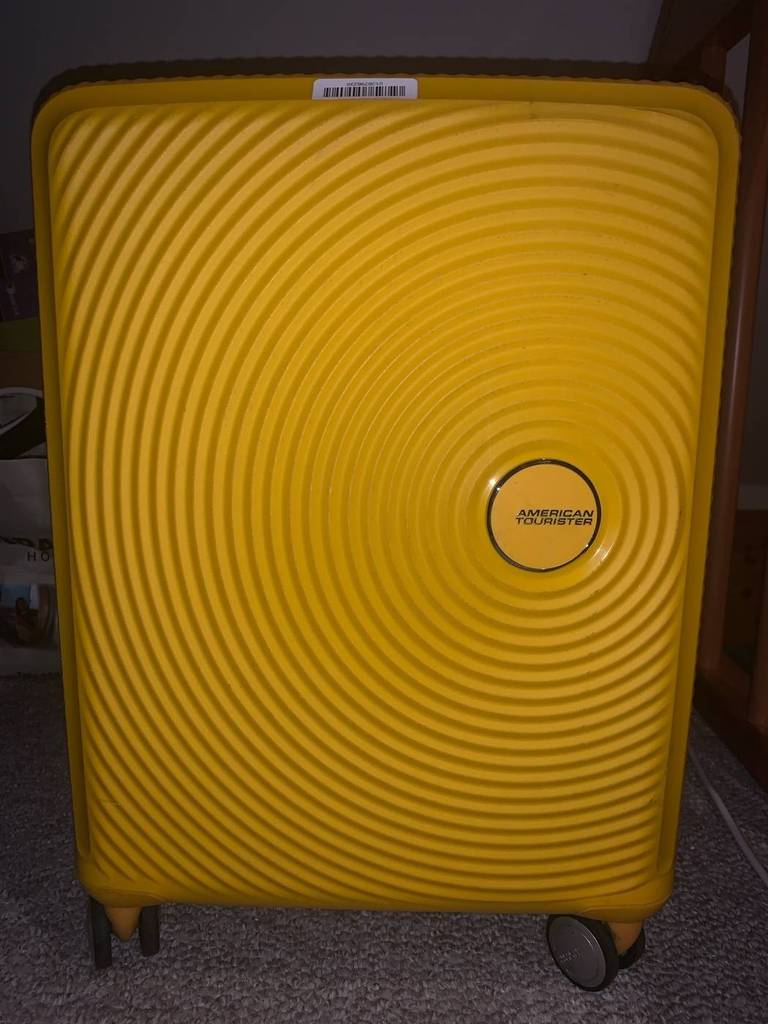 Nahaufnahme von vorn auf einen gelben American Tourister Handgepäck-Koffer im Test vor dunklem Hintergrund.