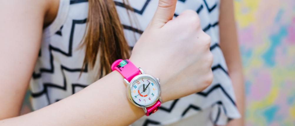 Ein Mädchen gibt ihrer analogen Kinderuhr ein Daumen-hoch-Zeichen: Die Kinderuhr hat den Kinderuhr-Test beim Mädchen bestanden