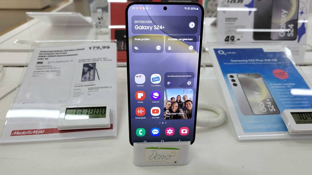 Ein Android-Smartphone steht mit eingeschaltetem Display zum Testen auf einem weißen Regaltisch.