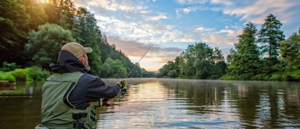 Angelhandschuhe im Test: Angler steht im Fluss und hält seine Angel.
