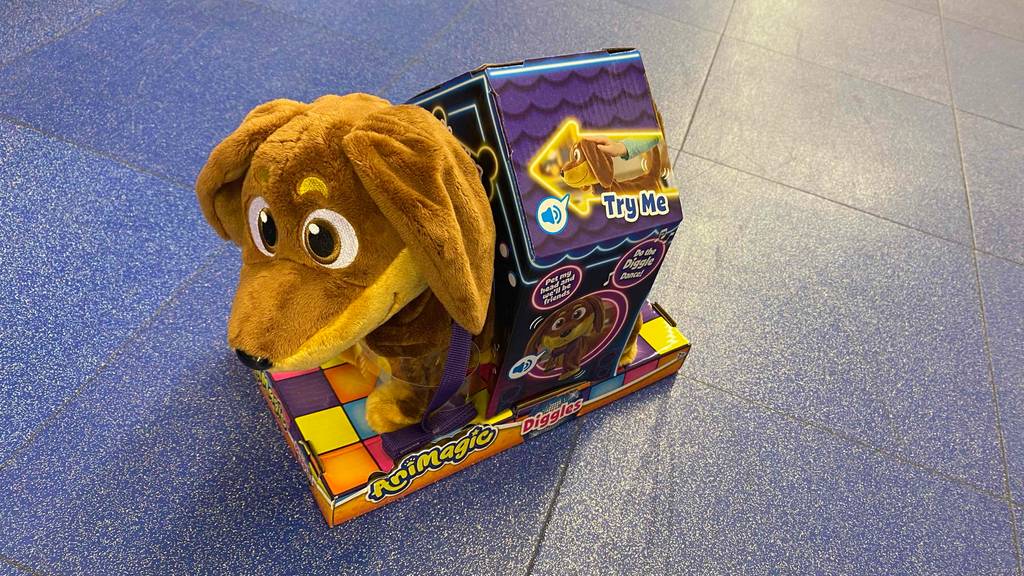 Getestet: Spielzeug-Hund, der läuft und bellt im Plüschdesign von schräg oben betrachtet. Das niedliche Kuscheltier befindet sich in seiner Verpackung auf einem blauen Fliesenboden.
