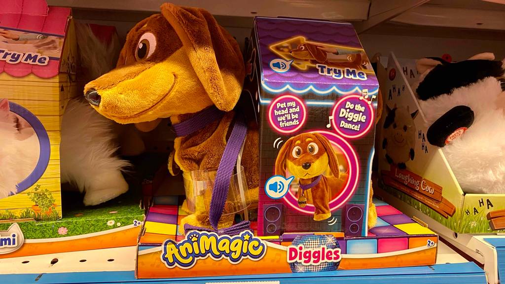 Seitenansicht eines getesteten Spielzeug-Hundes, der läuft und bellt in seiner Verpackung zwischen weiteren Plüschtieren auf einem Verkaufsregal.