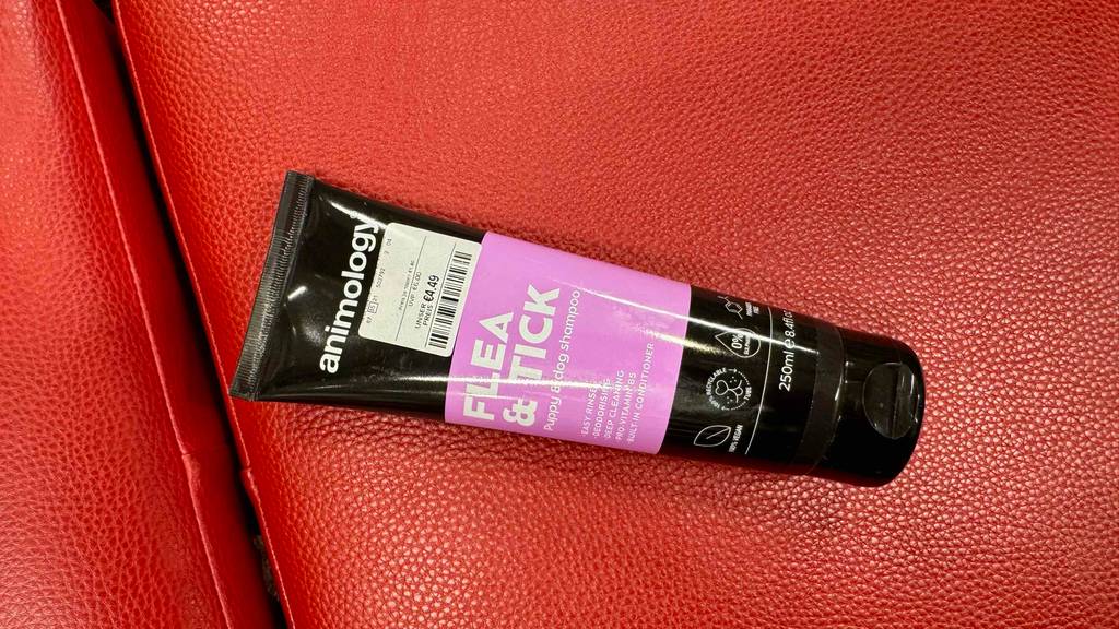 Eine Tube Flohshampoo für den Hund liegt zum testen auf einer roten Fläche.