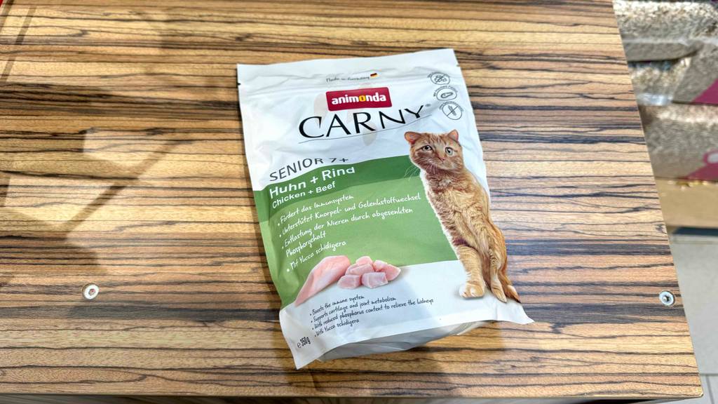 Eine Packung Katzenfutter senior liegt zum testen auf einer Holzfläche.