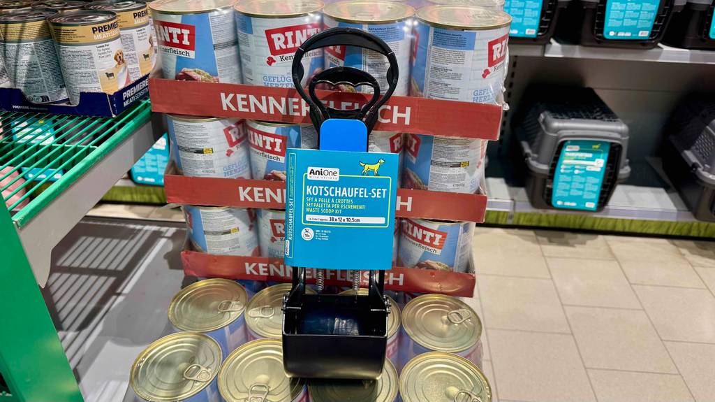 Eine getestete Hundekotschaufel steht auf mehreren Dosen Hundefutter.