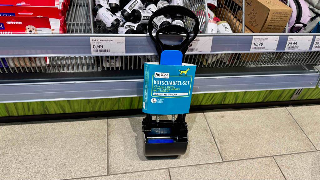 Eine Hundekotschaufel im Kartonblister steht zum testen vor einem Regal mit Kotbeuteln.