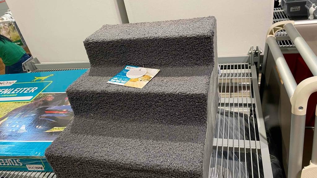 Vordere Ansicht einer grauen Anione-Hundetreppe im Test, die mit einem Plüsch-Stoff ausgestattet ist und über drei Stufen verfügt, auf einem Verkaufsregal.