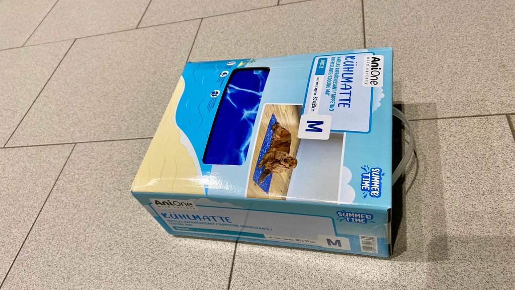 Kühlmatten für Hunde getestet: Kühlmatte in Größe M von Anione liegt in einer hellblauen Verpackung mit Sichtfenster auf einem Boden.