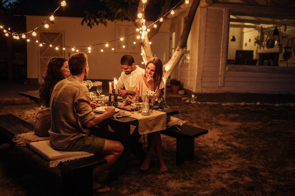Anker-Bluetooth-Lautsprecher im Test: Vier Erwachsene sitzen draußen unter Lichterketten und essen.