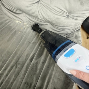 Der Anktel 601-N saugt mit Bürstenaufsatz Krümel aus einer grauen Polsterfläche.