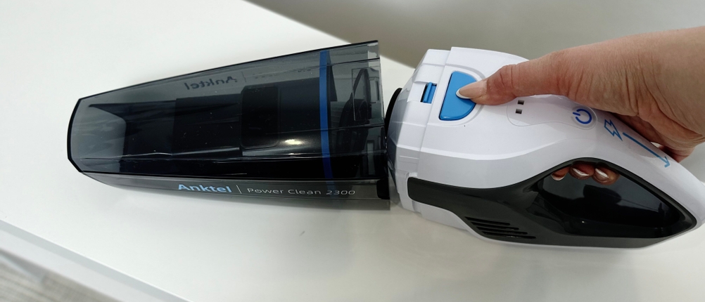 Eine Hand löst den Staubbehälter des Anktel 601-N mithilfe des blauen Entriegelungsknopfs.