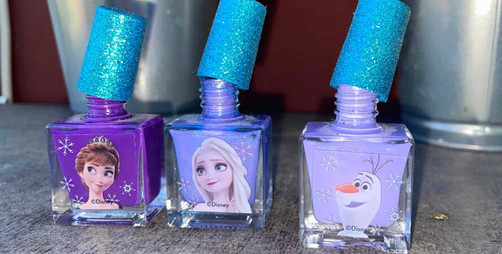 Drei getestete Nagellacke für Kinder stehen nebeneinander vor zwei Pflanzentöpfen.