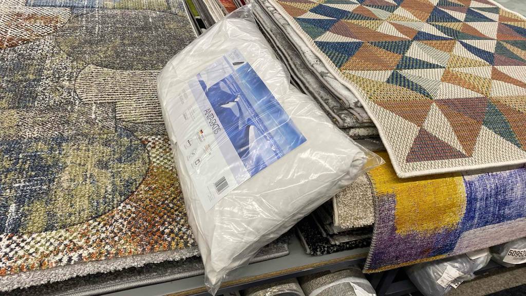 Ein eingepacktes Federkissen 80x80 im Test liegt hochkant auf einem Stapel Teppiche.
