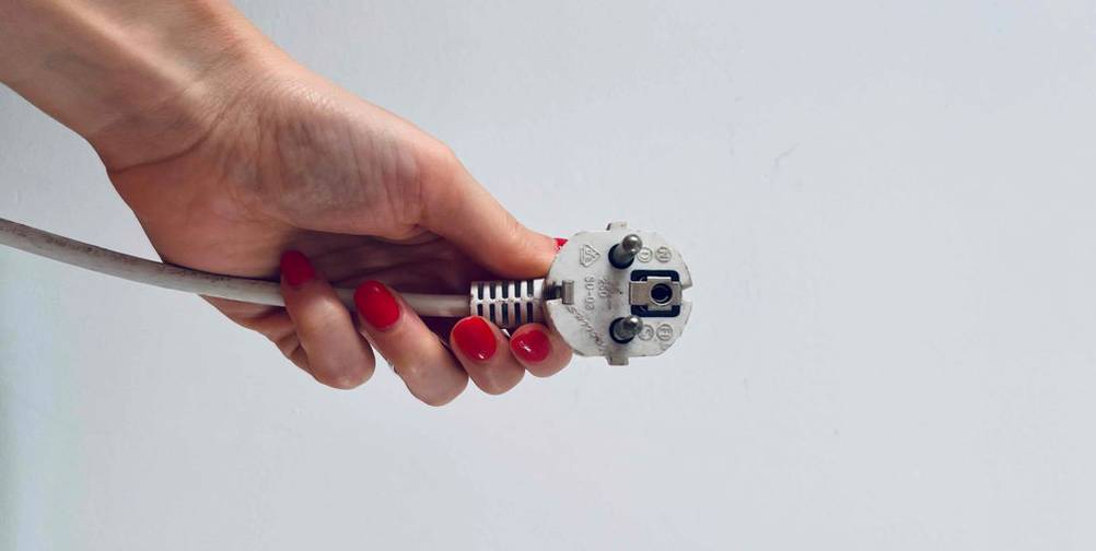 Eine Hand hält den Schuko-Stecker eines getesteten Bodenventilators vor einem weißen Hintergrund.