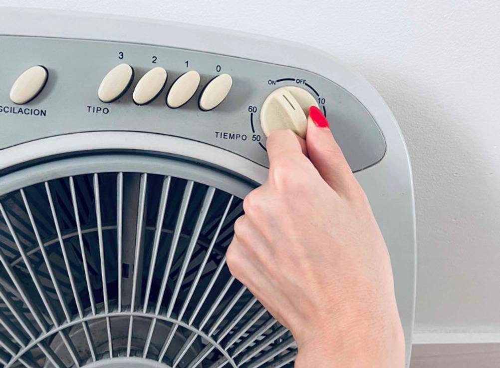 Eine Hand stellt an einem Drehregler die Laufzeit des getesteten Bodenventilators ein.
