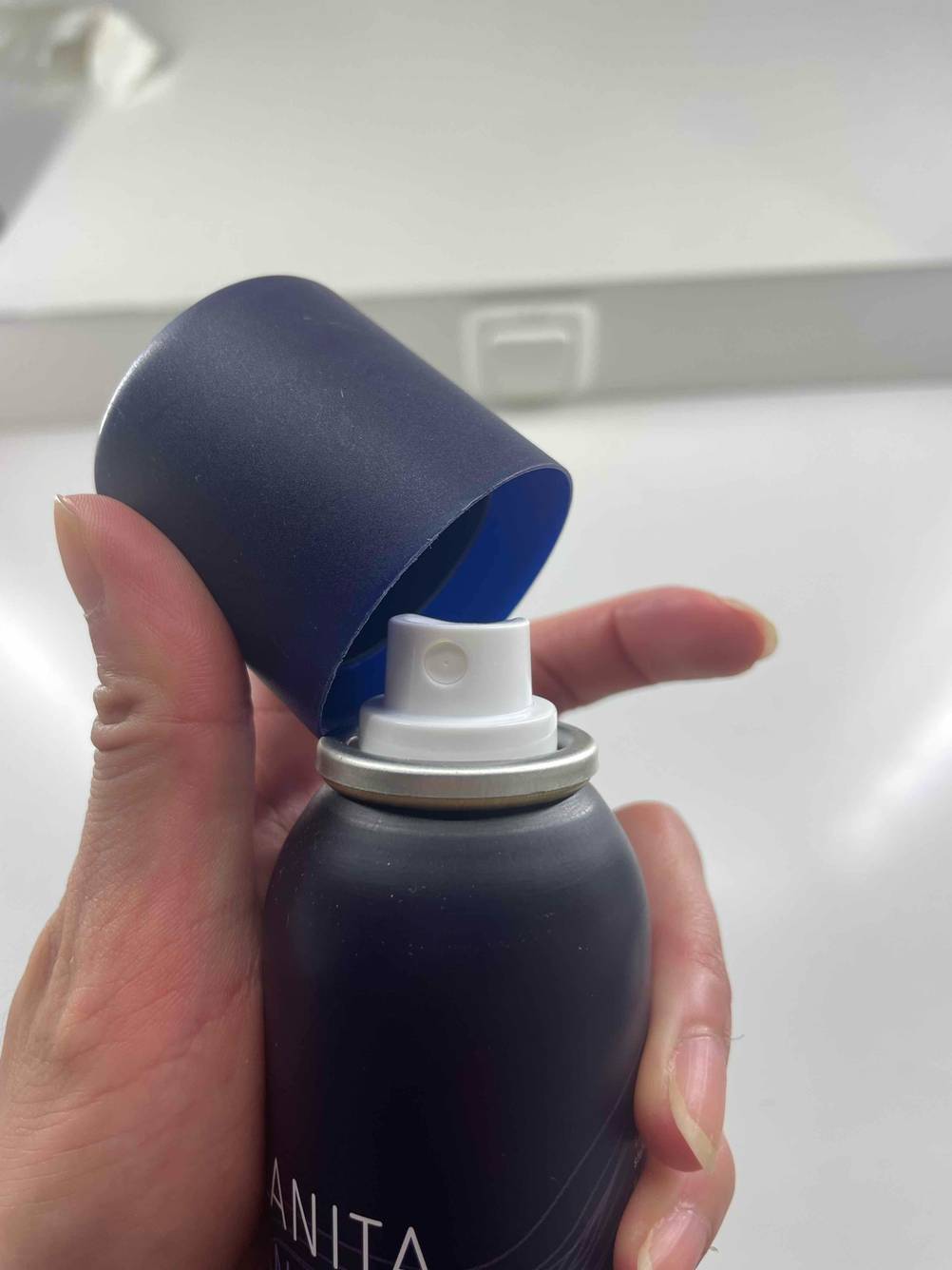 Eine Hand nimmt die Kappe einer Dose des getesteten Antistatik-Sprays ab.