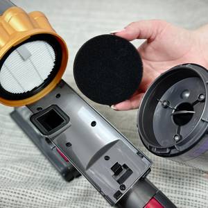Die Einzelteile des Filtersystems vom Anyson Stars 5 sind ausgebaut. Eine Hand hält den schwarzen Schaumstofffilter.