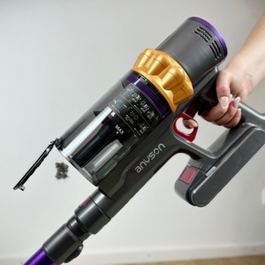 Der Staubbehälter des Anyson Stars 5 ist geöffnet. Staub fällt sichtbar heraus, während eine Hand das Gerät hält.