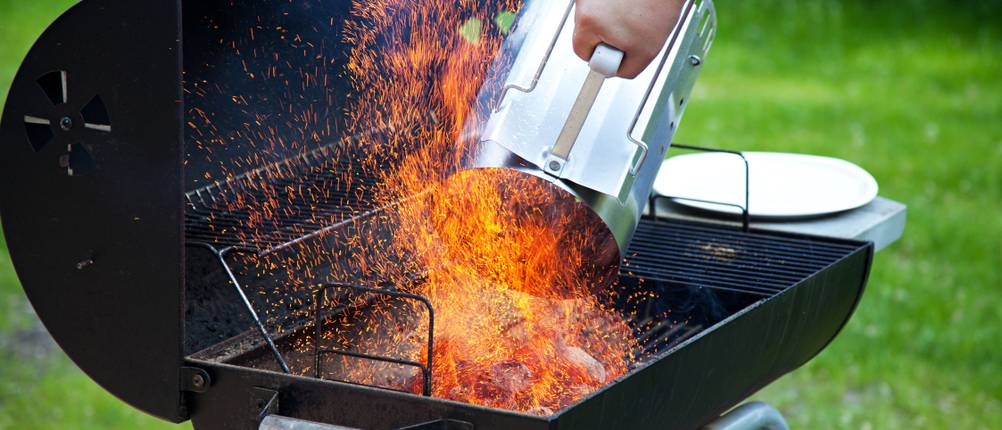 Glühende Grillkohle wird aus einem Anzündkamin in einen Grill gekippt.