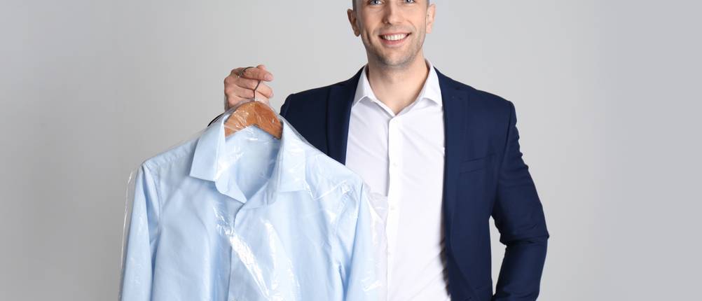 Anzugtaschen im Test: Mann hält Kleiderbügel mit Hemd in Plastiktüte auf hellgrauem Hintergrund