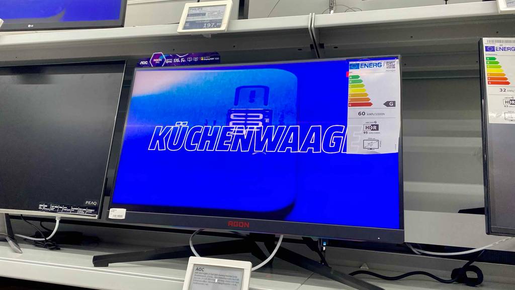 Gaming-Monitore im Test: ein eingeschaltetes AGON-Modell inklusive Energieeffizienzlabel steht zwischen weiteren Monitoren auf einem Verkaufsregal.