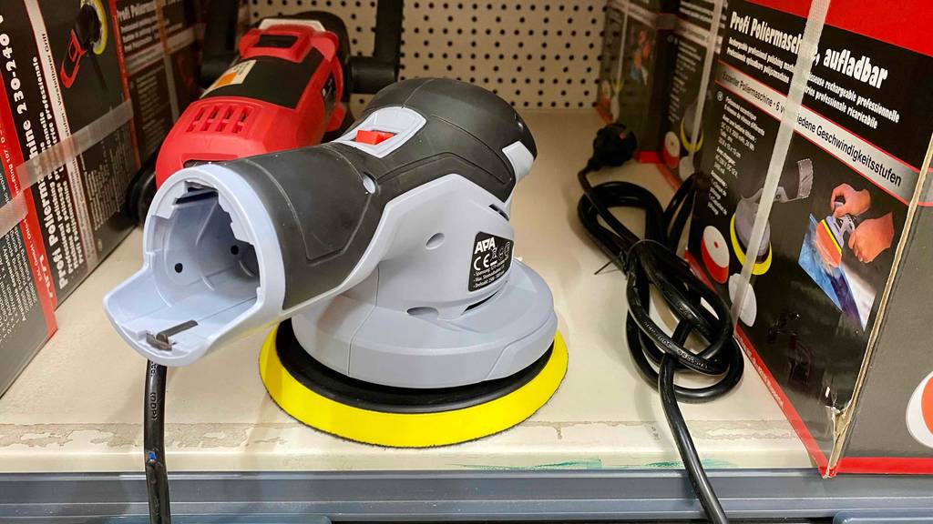 Ansicht auf den Anschluss für den Akku einer im Verkaufsregal neben ihrer Verpackung stehenden, hellgrauen, getesteten Akku-Poliermaschine.