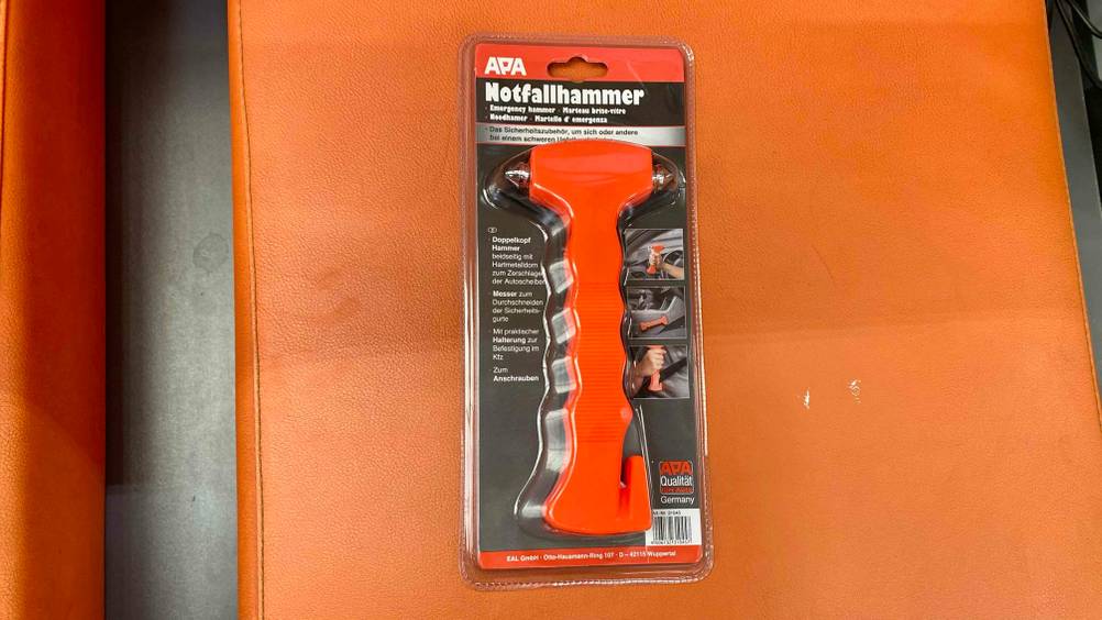 Ein getesteter Notfallhammer in seiner Originalverpackung auf einer orangen Fläche.