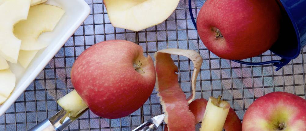 Apfelausstecher im Test: Geschnittene, entkernte und geschälte Äpfel liegen neben Küchenhelfern auf einem Gitter.