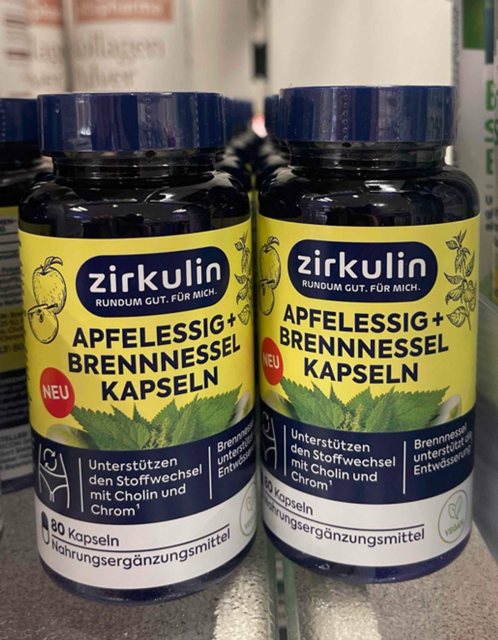 Zwei lichtdichte Kunststoffdosen der getesteten Apfelessig-Kapseln stehen nebeneinander auf einem Regal.