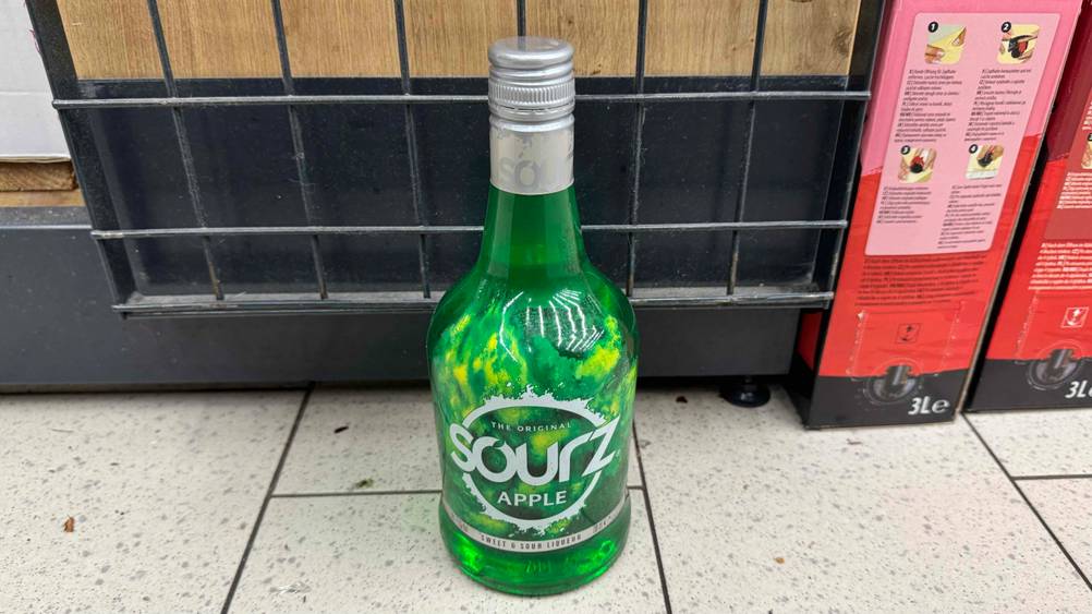 Eine Flasche Apfellikör im Test von leicht oben auf einem Fließenboden stehend.