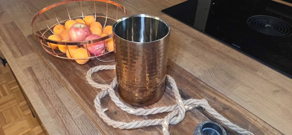 Weinkühler von Apollo steht auf Holztisch mit Dekoartikeln und Schale mit Äpfeln.
