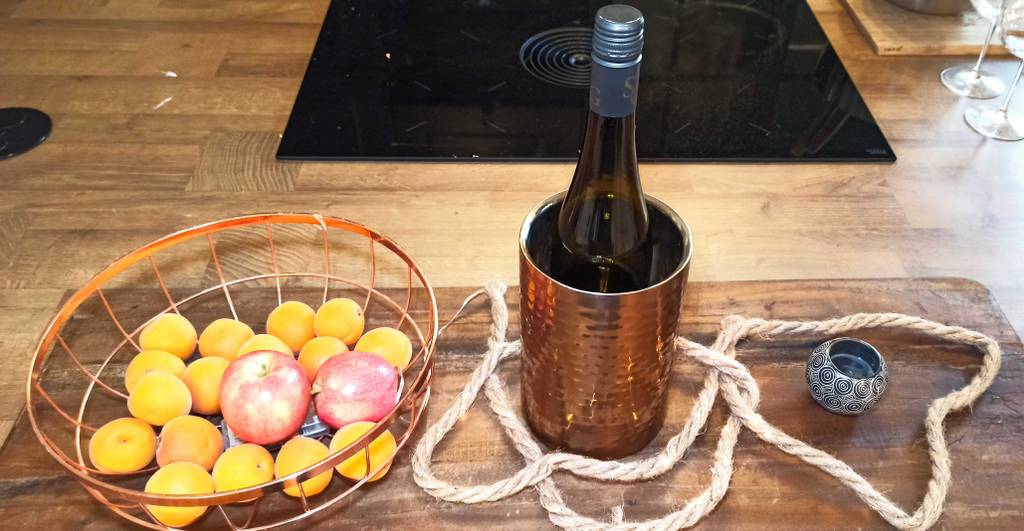 Im Test: Ein mit einer Weinflasche gefüllter Weinkühler steht zwischen Obst und einem Teelichthalter auf einem Holztisch.