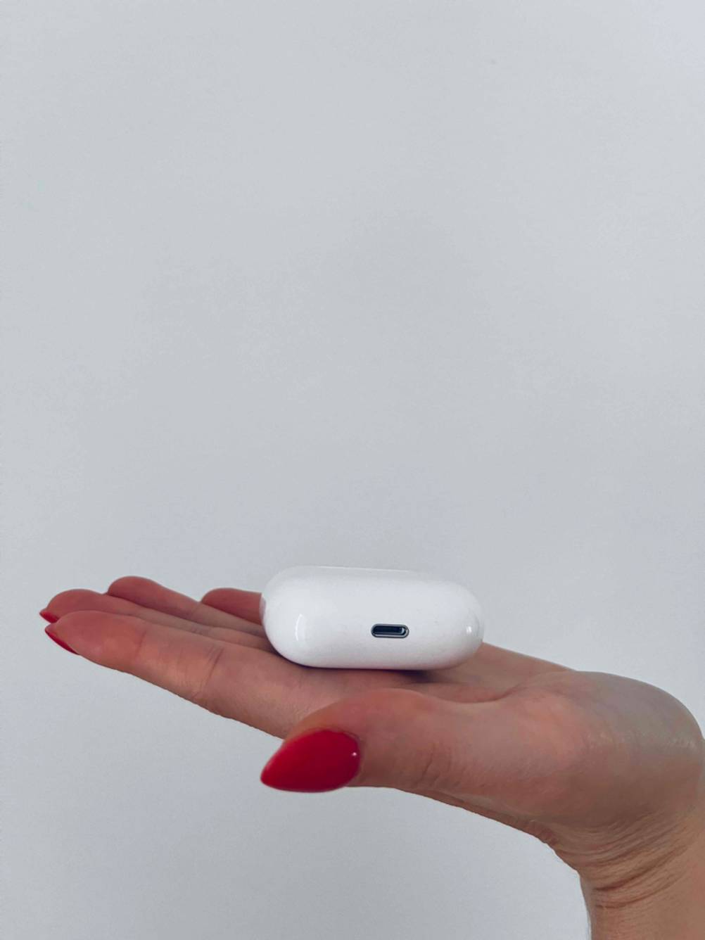 Hand hält ein geschlossenes, weißes, getestetes In-Ear-Headset vor einen hellen Hintergrund.