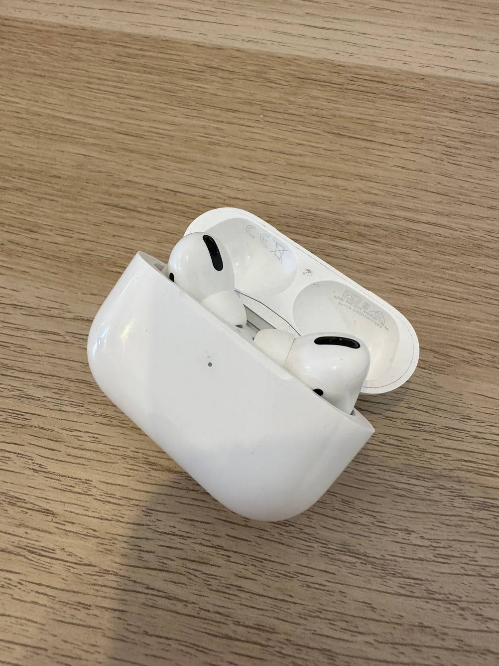 Eine geöffnete Box, aus der Wireless In-Ear-Kopfhörer herausschauen, liegt auf einem Holzuntergrund.