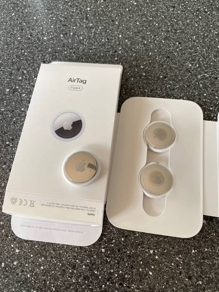 Ein 4er-Pack Apple AirTag Schlüsselfinder im Test liegt in geöffneter weißer Verpackung auf einem grauen Untergrund.