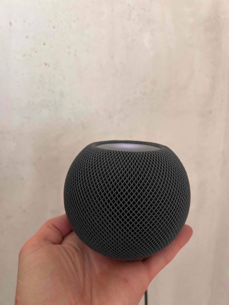 Eine Hand hält einen getesteten AirPlay-Lautsprecher vor eine helle Wand.