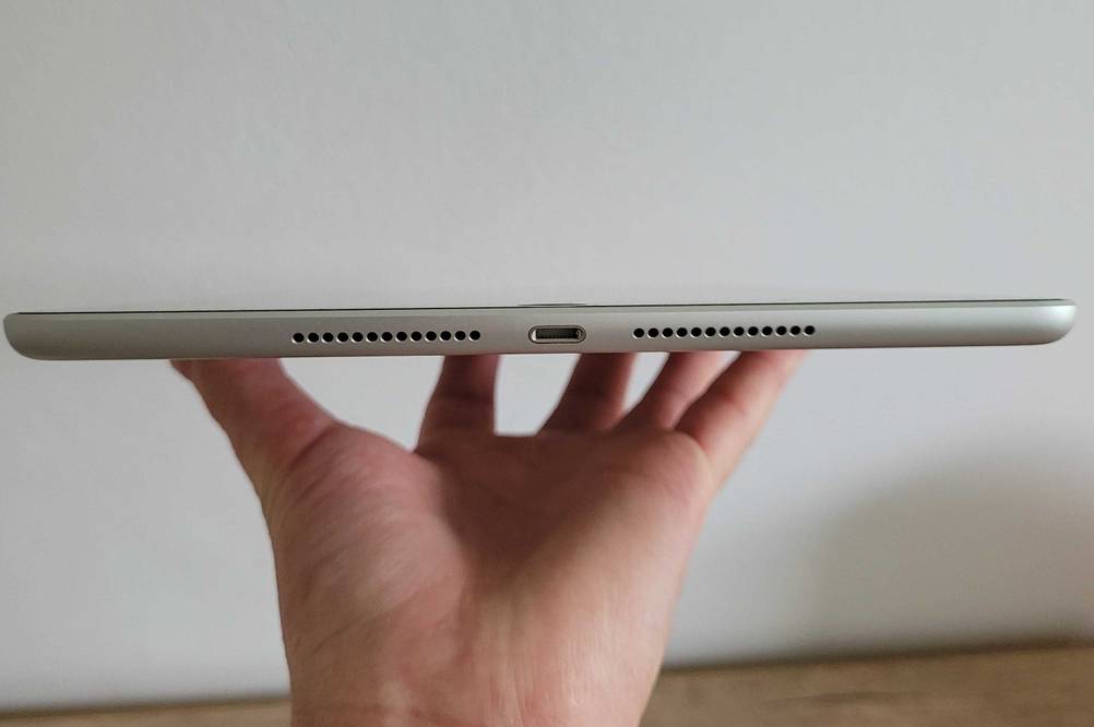 Eine Hand hält ein Apple iPad im Test mit dem Anschluss nach vorne flach vor eine helle Wand.