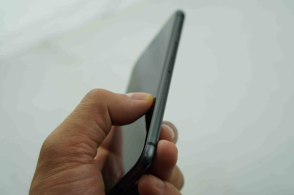 Hand hält, mit Blick auf die Seite, schwarzes getestetes Smartphone vor hellem Hintergrund.
