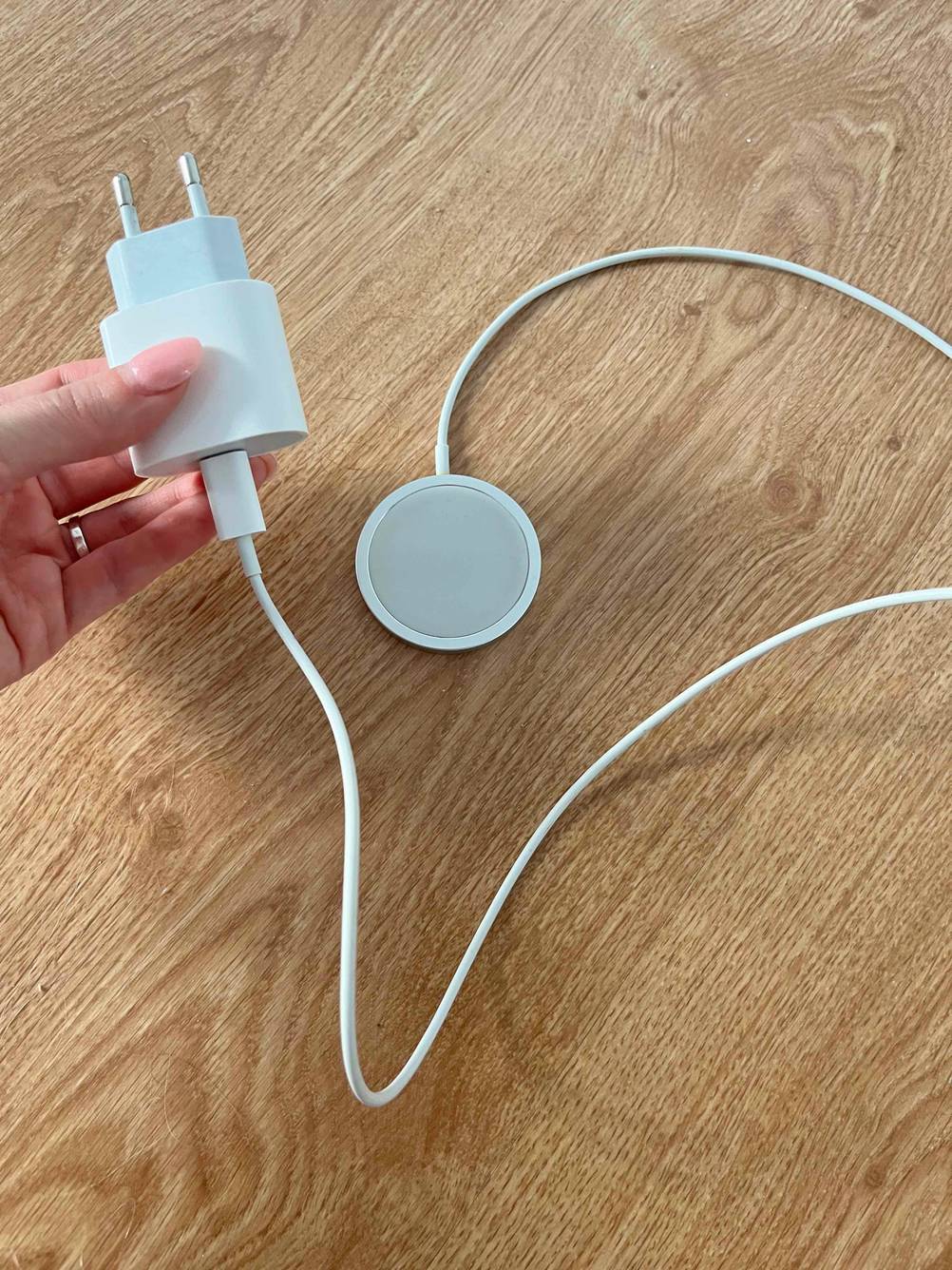 Magnet-Ladekabel im Test: Hand hält den Netzstecker eines Apple-Magnet-Ladekabels, das auf einem Holzboden liegt.