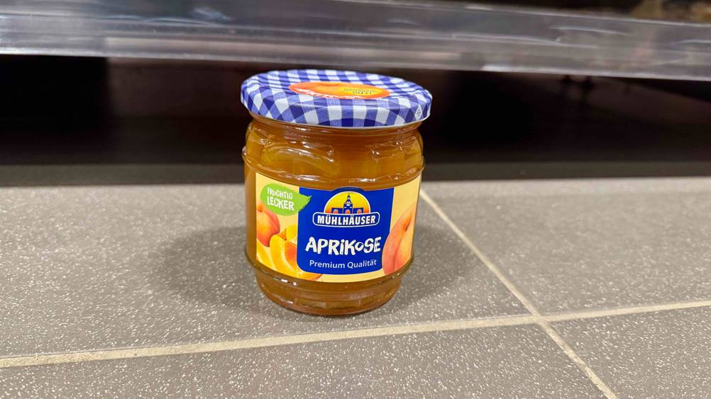 Ein Glas Aprikosenmarmelade im Test auf einem grauen Boden stehend.